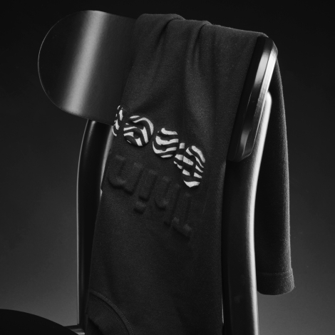 T-shirt oversize noir posé sur le dossier d'une chaise avec un marquage visible au centre de la poitrine.