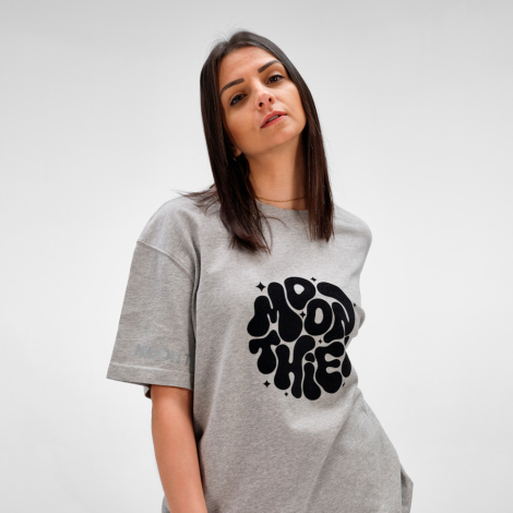 Femme portant un t-shirt oversize gris avec un marquage visible au centre de la poitrine.