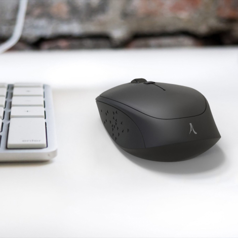 Souris sans fil noire en situation d’utilisation sur un bureau à côté d’un clavier, sans marquage publicitaire visible.