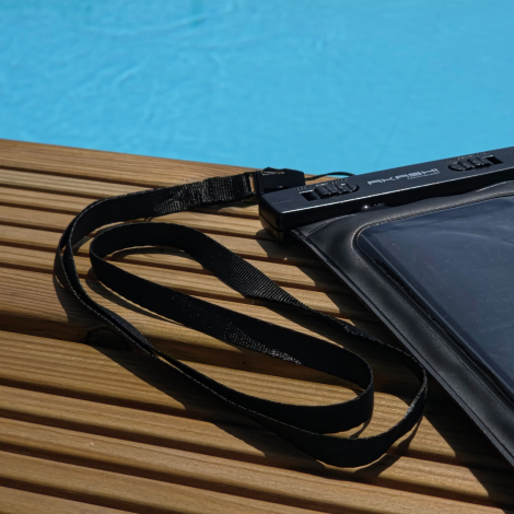 Gros plan de la pochette et de sa dragonne posées au bord d’une piscine, avec vue sur le système de fermeture à double verrouill