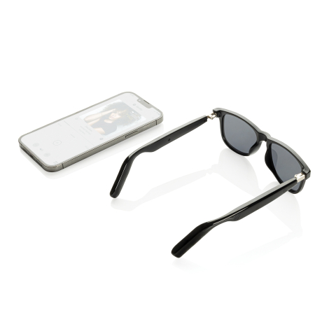 Smartphone placé à côté des lunettes audio ouvertes, illustrant leur utilisation avec un appareil mobile.
