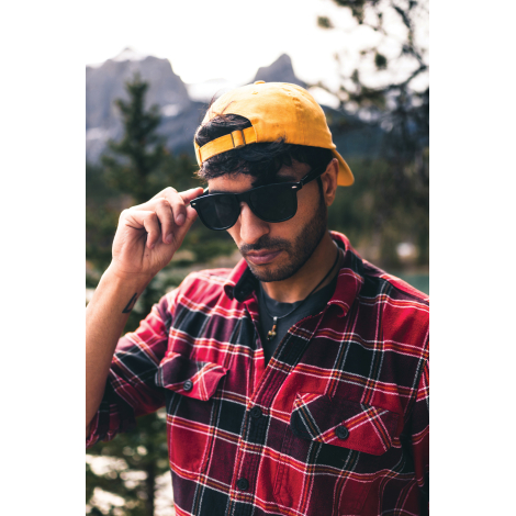 Homme portant les lunettes audio en extérieur et ajustant la monture d'une main, dans un environnement naturel.