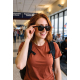 Femme portant les lunettes audio dans un terminal d'aéroport, la main posée sur la branche des lunettes.