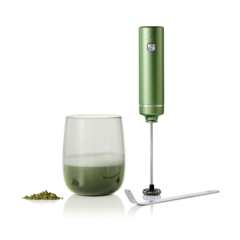 Mousseur électrique vert retourné au-dessus d’un verre contenant une boisson verte mousseuse, avec cuillère métallique et poudre