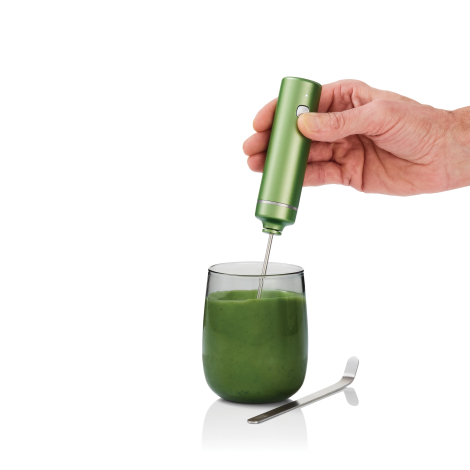 Mousseur électrique vert tenu à la main au-dessus d’un verre rempli d’une préparation verte homogène, avec cuillère métallique p