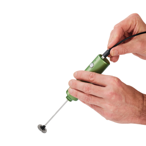 Gros plan sur le mousseur électrique vert tenu à deux mains pendant le branchement d’un câble sur sa partie supérieure.