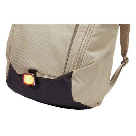 Détail de la partie basse avant d’un sac à dos beige avec empiècement foncé et petit éclairage fixé sur une sangle.