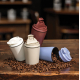 Mise en scène de quatre tasses à café blanches, beige, rouge et bleu clair sur une table en bois couverte de grains de café, don