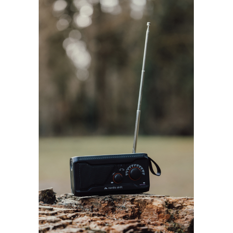 Radio multifonctions posée sur une souche en extérieur avec antenne télescopique déployée, dragonne latérale et logo de la gamme