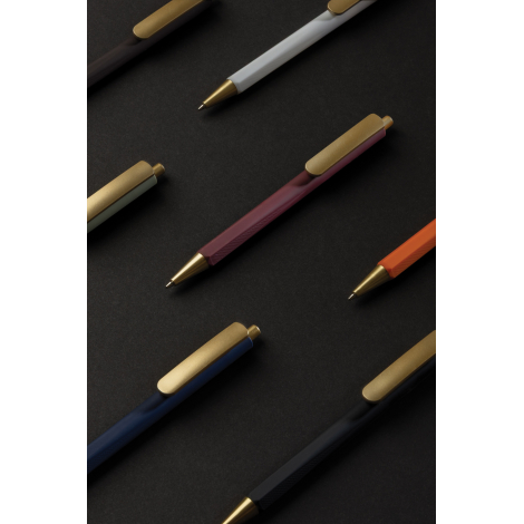 Composition de plusieurs stylos à trois faces disposés en diagonale sur fond noir, dans différents coloris dont bordeaux, blanc,