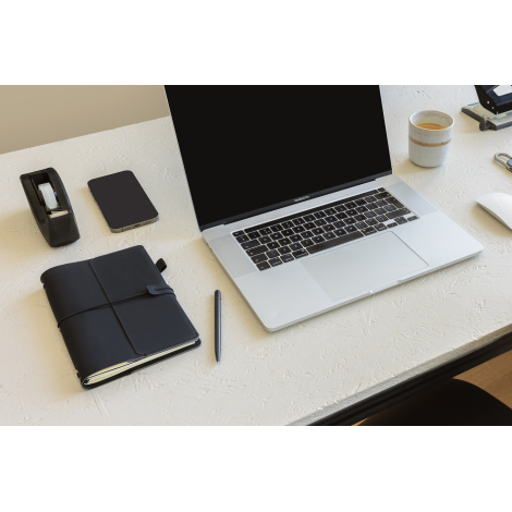 Carnet organiseur noir posé sur un bureau à côté d’un stylo, d’un ordinateur portable, d’un smartphone, d’un dérouleur adhésif e