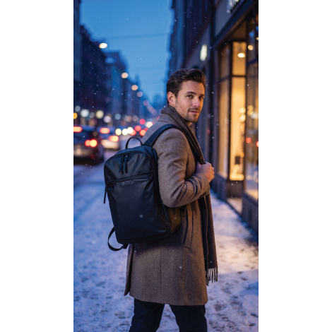 Homme portant le sac à dos noir sur les épaules dans une rue enneigée, avec vue de trois quarts sur la face avant du sac.