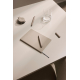 Carnet de notes beige fermé posé sur une table avec un stylo, un verre d’eau et de petits accessoires, son ruban marque-page noi Carnet de notes beige fermé posé sur une table avec un stylo, un verre d’eau et de petits accessoires, son ruban marque-page noi