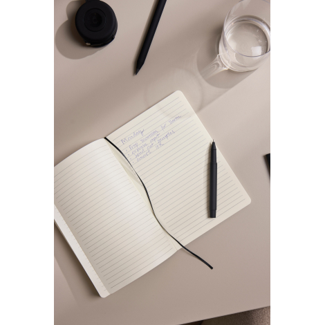 Carnet de notes ouvert sur des pages lignées avec des notes manuscrites, accompagné d’un stylo noir et d’un verre d’eau sur une 