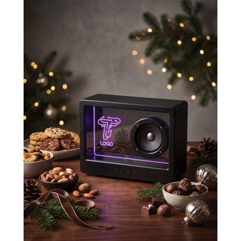 Enceinte noire mise en scène sur une table en bois parmi des chocolats, fruits secs, branches de sapin et décorations, avec écla