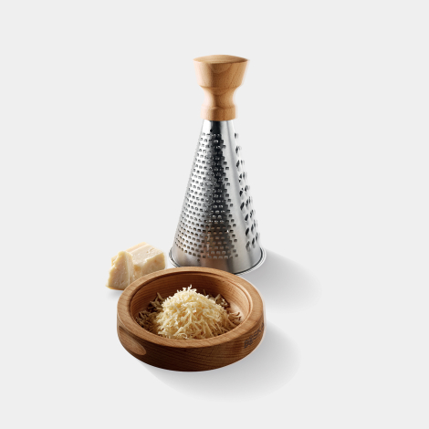 Râpe conique avec poignée en bois placée derrière son support en bois contenant du fromage râpé, avec un morceau de fromage posé