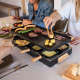 Appareil à raclette en cours d’utilisation lors d’un repas, avec aliments grillés sur la plaque supérieure et plusieurs poêlons Appareil à raclette en cours d’utilisation lors d’un repas, avec aliments grillés sur la plaque supérieure et plusieurs poêlons