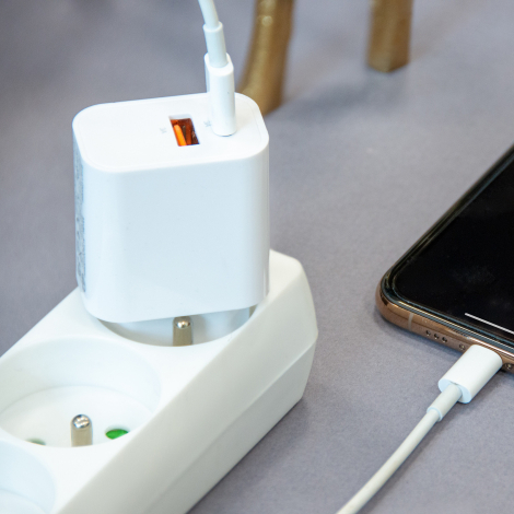 Chargeur secteur blanc branché sur une multiprise, vu de trois quarts, avec deux câbles connectés sur sa partie supérieure et un