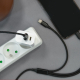 Chargeur secteur blanc branché sur une multiprise et vu du dessus, avec un câble noir connecté à l’un des ports et un second por