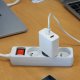 Chargeur secteur blanc branché sur une multiprise et relié à un câble USB-C, dans un environnement de bureau. Aucun marquage vis Chargeur secteur blanc branché sur une multiprise et relié à un câble USB-C, dans un environnement de bureau. Aucun marquage vis