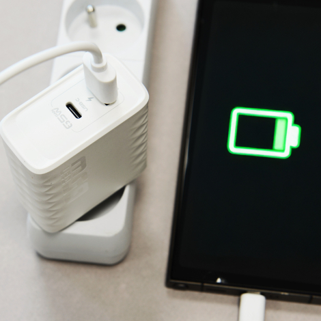Chargeur secteur blanc branché sur une multiprise et relié par câble à un appareil dont l’écran affiche un symbole de batterie e