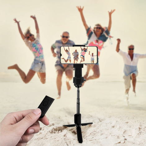 Perche à selfie noire utilisée en configuration trépied sur une plage, avec smartphone en position horizontale. Une télécommande