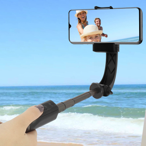 Perche à selfie noire déployée et tenue à la main devant une plage, avec smartphone en position horizontale. Aucun marquage visi
