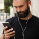 Écouteurs filaires blancs portés par une personne consultant son smartphone en extérieur. Aucun marquage visible.