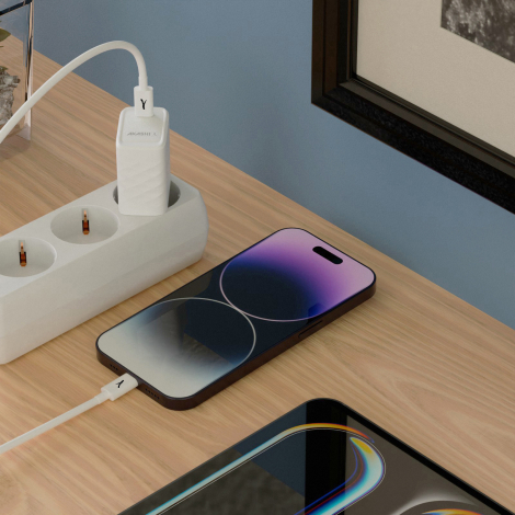 Chargeur secteur blanc branché sur une multiprise et relié par un câble à un téléphone posé sur une surface en bois, avec un sec