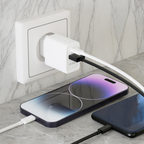 Chargeur secteur blanc branché sur une prise murale, avec deux câbles connectés à sa face avant et deux téléphones posés à proxi