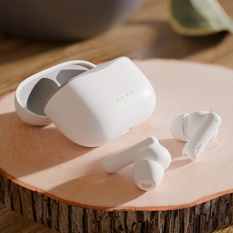 Boîtier de charge blanc ouvert et deux écouteurs blancs disposés à proximité sur une surface en bois. Quatre indicateurs lumineu