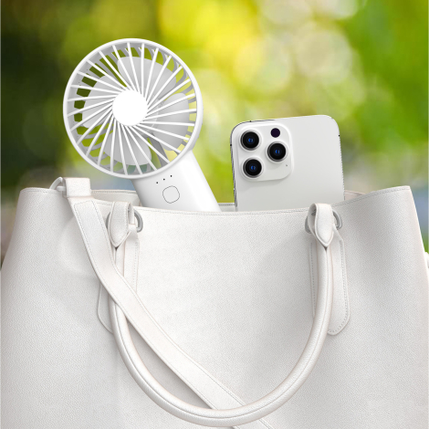 Mise en situation du ventilateur portable glissé dans un sac à main aux côtés d’un smartphone, illustrant son format nomade.