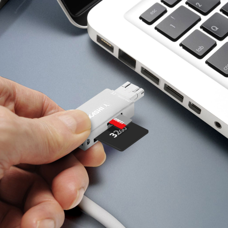Lecteur de cartes tenu en main à proximité d’un ordinateur portable, avec une carte SD et une carte micro SD insérées dans les l