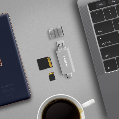 Lecteur de cartes posé entre un smartphone, un ordinateur portable et une tasse, accompagné d’une carte SD, d’une carte micro SD