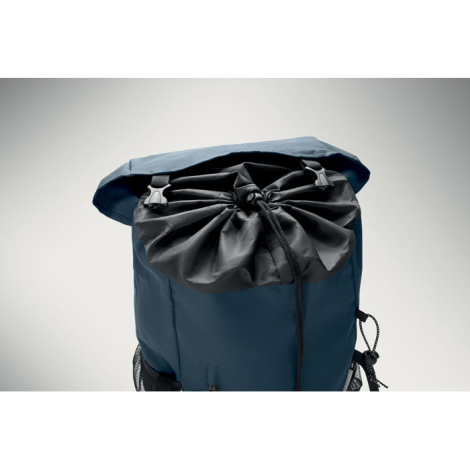Le rabat du sac à dos bleu est relevé pour montrer l’ouverture du compartiment principal, resserrée par un cordon avec système d