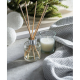 Diffuseur à bâtonnets et bougie mis en scène côte à côte dans une ambiance intérieure claire, près d’un textile gris et de branc Diffuseur à bâtonnets et bougie mis en scène côte à côte dans une ambiance intérieure claire, près d’un textile gris et de branc
