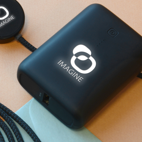 Gros plan sur une batterie de secours noire personnalisée avec un logo blanc rétroéclairé, posée sur une surface colorée.