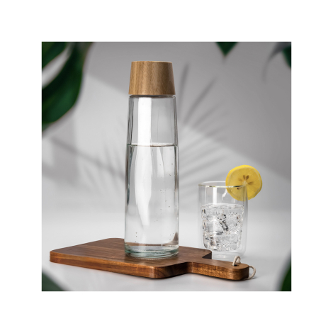 Bouteille en verre avec bouchon aspect bois posée sur une planche avec un verre d’eau citronnée.