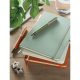Plusieurs carnets A5 colorés sont empilés sur une table, avec un carnet vert au-dessus accompagné de deux stylos, tandis que des