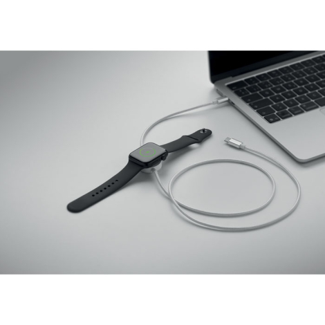 Câble blanc branché à un ordinateur portable et utilisé pour charger une montre connectée posée sur son module circulaire.