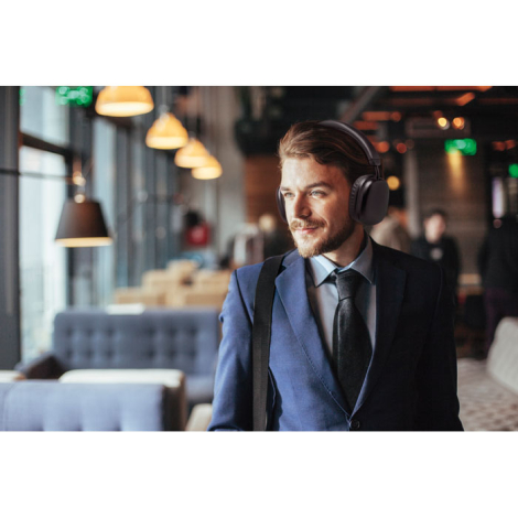 Un homme en costume porte le casque audio noir sur les oreilles dans un espace intérieur aménagé avec tables et banquettes.