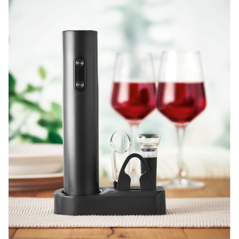 Tire-bouchon électrique noir et ses accessoires installés sur leur base, mis en scène devant deux verres de vin.