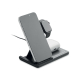 Station de charge noire avec un smartphone placé sur le support incliné, une montre connectée à l’arrière et un boîtier d’écoute Station de charge noire avec un smartphone placé sur le support incliné, une montre connectée à l’arrière et un boîtier d’écoute