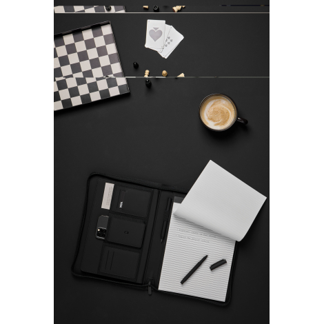 Porte-documents noir ouvert posé sur un bureau, avec bloc-notes ligné, stylo et plusieurs accessoires rangés dans les compartime