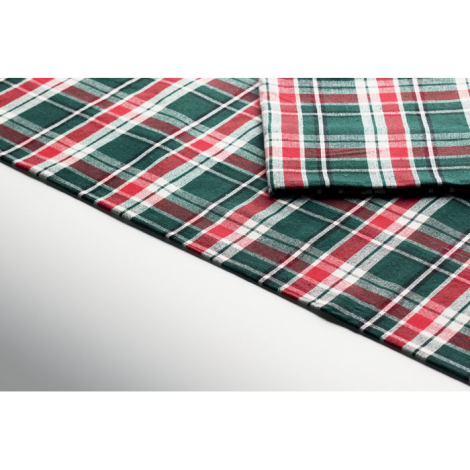 Gros plan sur le tissu à carreaux verts, rouges et blancs de la nappe et d’une serviette assortie, montrant les bordures cousues