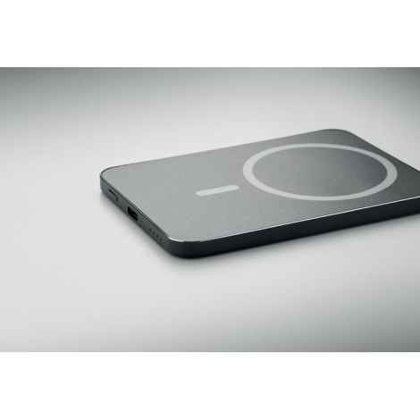 Batterie externe noire présentée à plat en perspective, avec cercle et repère gris sur sa face supérieure, port USB-C et voyants