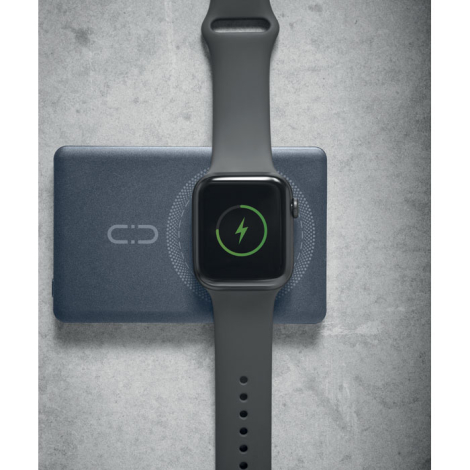 Montre connectée noire posée sur la zone circulaire d’une batterie externe bleu foncé, avec symbole de charge vert affiché sur s
