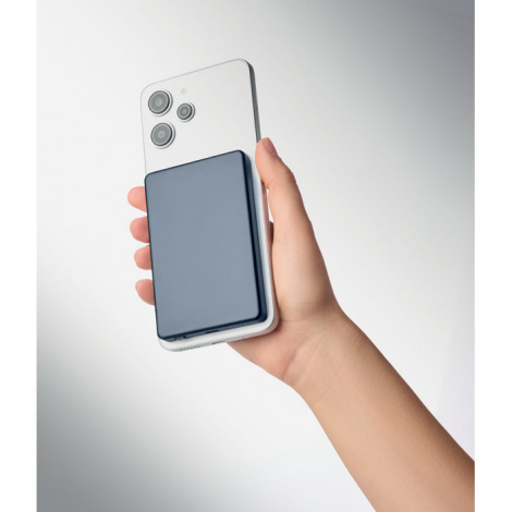 Smartphone blanc tenu en main avec batterie externe bleu foncé rectangulaire fixée au dos de l’appareil.