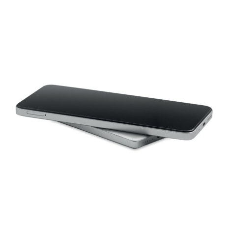 Smartphone noir posé en biais sur une batterie externe argentée, laissant apparaître les tranches des deux appareils sur fond bl