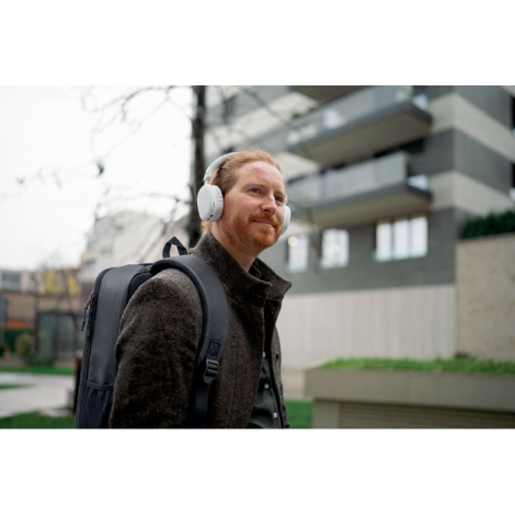 Un homme portant le sac à dos noir sur les deux épaules marche à l’extérieur avec un casque audio blanc sur les oreilles.